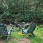 The creek has chairs and outdoor tables to write on, as well as walking paths Two empty green chairs facing a small creek, surrounded by trees