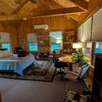 Interior of a small writing cabin, featuring the bed and many windows
